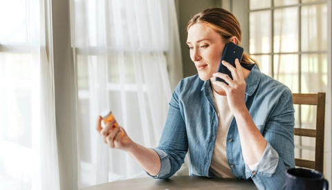 Woman is at home, she is communicating with the doctor via mobile phone while holding a bottle of medicine in her hand.