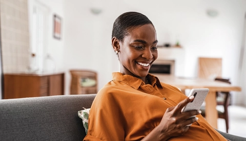 A pregnant woman smiles while looking at her mobile phone