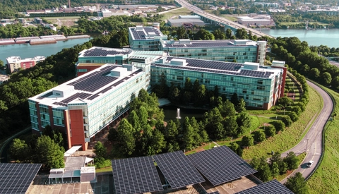 Aerial image of the BlueCross BlueShield of Tennessee campus showing solar‑equipped glass office buildings, surrounding trees, a small fountain pond, and the river and highways in the distance.