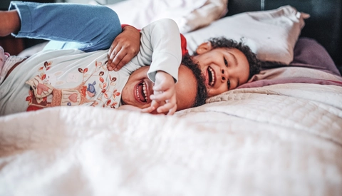 A brother and sister wearing pajamas excitedly laughing and hugging on a bed