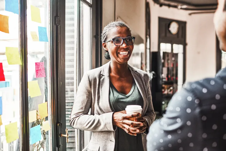 Smiling woman talking with her colleague while having coffee