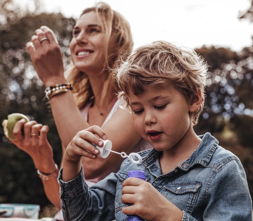 Small kid playing with bubbles at the park with his mother