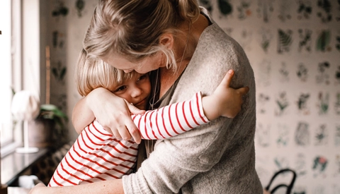 Loving daughter embracing mother while sitting on kitchen counter at home