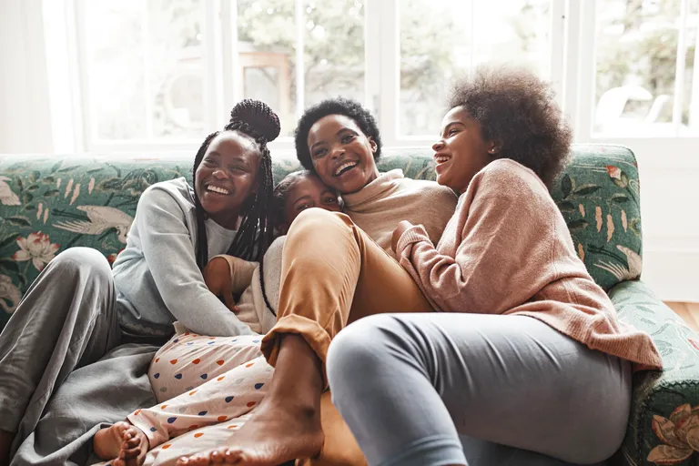 Happy young woman embracing and laughing while sitting on sofa at home