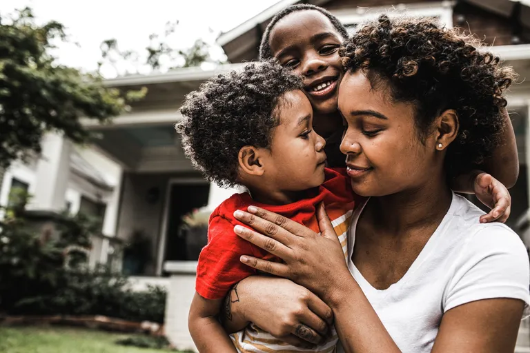 Mother playing with young sons in front of house