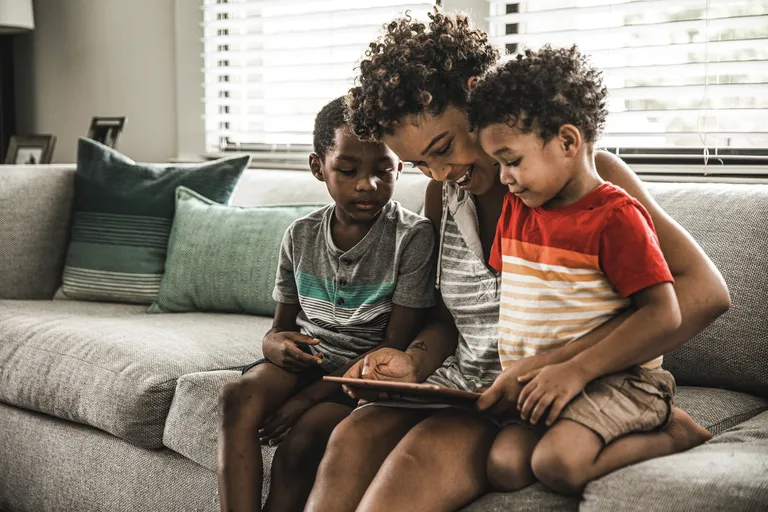 Single mother using tablet with young sons on couch