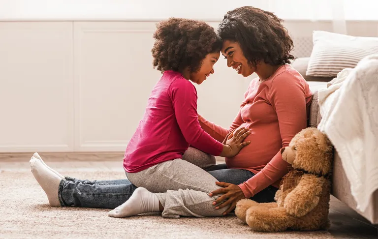 Smiling mother with her toddler happily resting on her pregnant belly