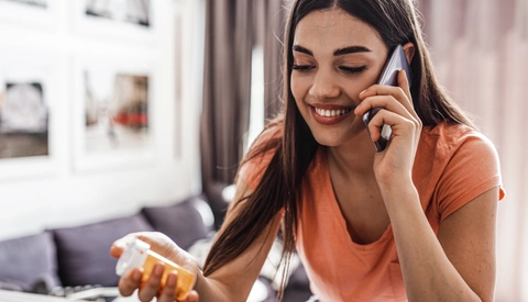 Young woman holding prescription pill bottle while talking on phone