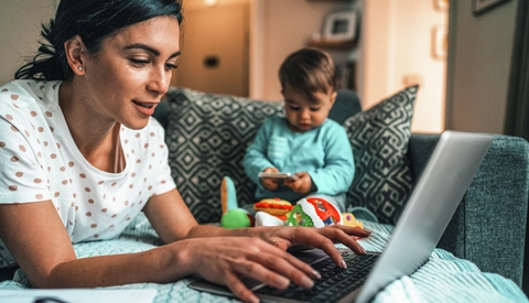 Young mother using laptop computer with baby nearby