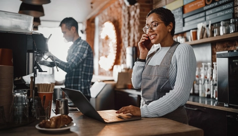 Smiling woman in a coffee shop using her phone and laptop