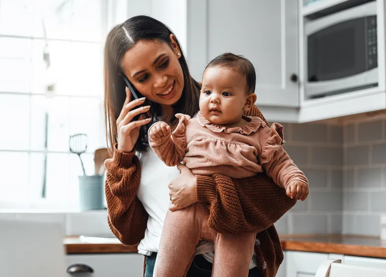 Young woman carrying her newborn baby while working at home
