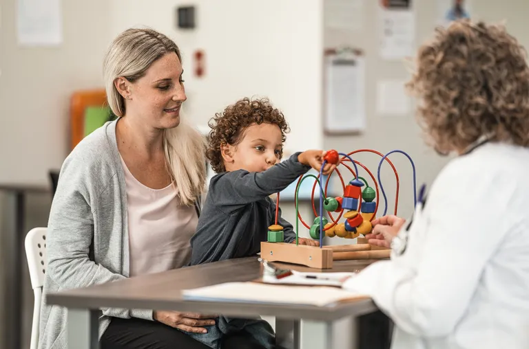 LIttle boy plays with toy while mother talks to pediatrician