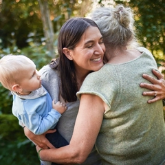 Three people outdoors sharing an embrace while one adult holds a young child in a natural setting.