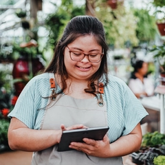 A young woman with Down syndrome working in a flower shop processing orders on an iPad.