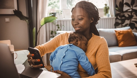 Younger mother holding her sleeping baby while looking at her phone