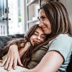 Young girl and mother hug each other on the couch 
