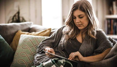 A woman relaxing on her couch while she looks at a iPad.