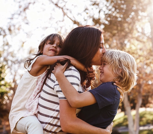 Mother carrying son and daughter as they play in park