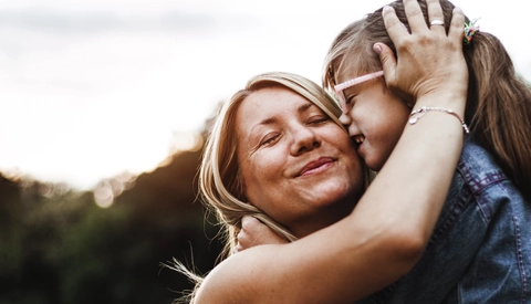 Mother and daughter embracing outdoors with sunset behind them
