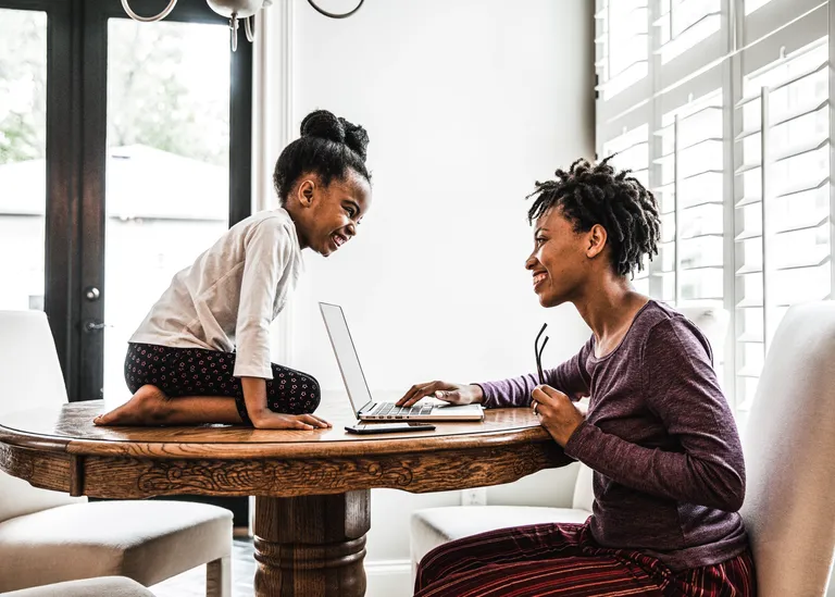 Mother working on laptop, daughter on table