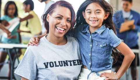 Happy volunteer poses with an elementary age female at a community event