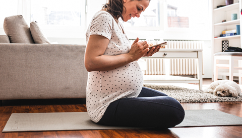 Pregnant woman sitting on the floor in living room, looking at her mobile phone.