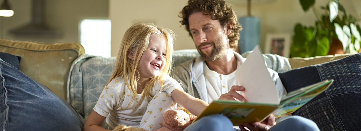 Father and daugther on a couch reading a book