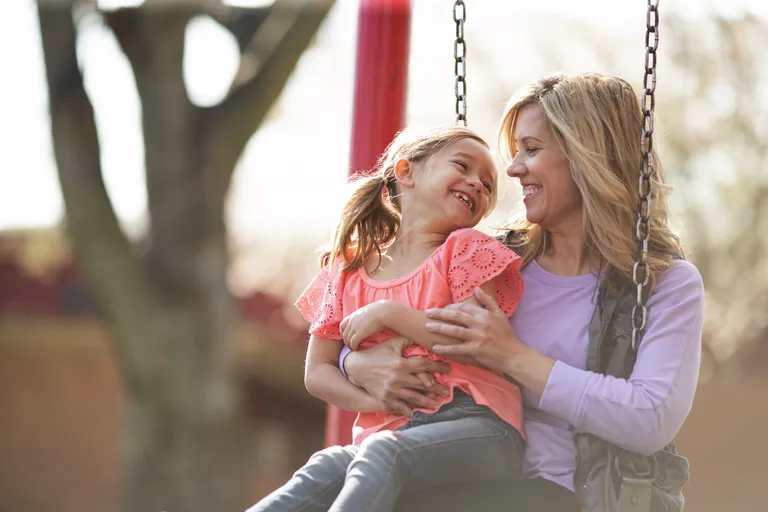Mother with daughter on swing on playground