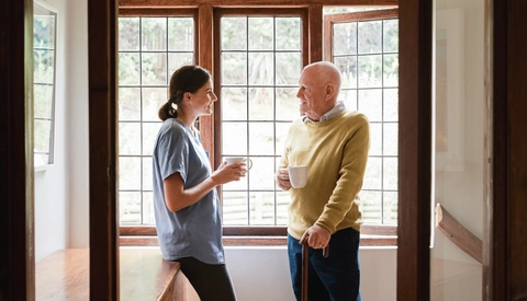A senior man and a young nurse having tea while chatting in a retirement home