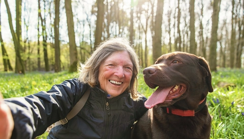A senior lady takes a selfie her with chocolate labrador dog.