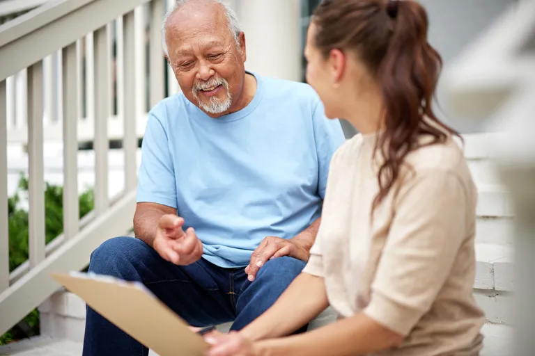 Smiling senior man with caregiver reviewing documents. Sitting outside at home on front steps.