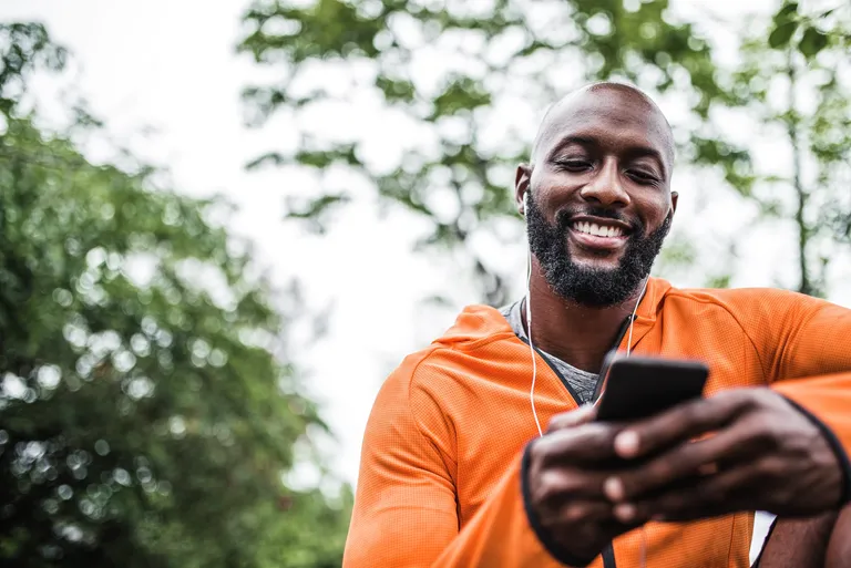Man sitting outdoors holding mobile phone getting ready for exercise