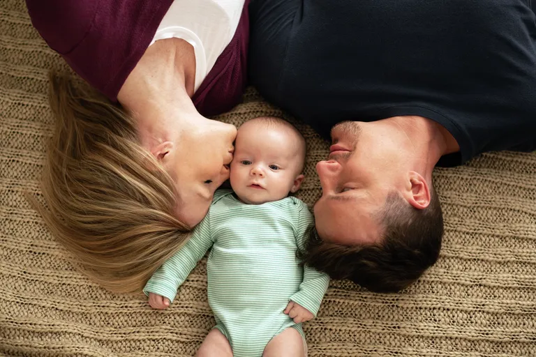 Mother and father laying next to newborn baby at home