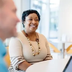 Employee seated at a table in a modern office space, wearing professional attire in a bright, contemporary setting.