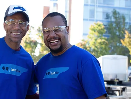 Two volunteers in matching blue Team Blue shirts stand together at an outdoor community service event.