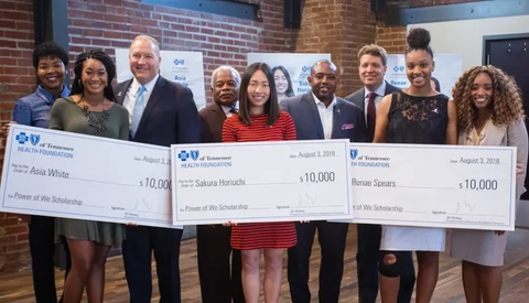 Scholarship recipients and organizers pose together indoors holding large award checks at a formal presentation event.