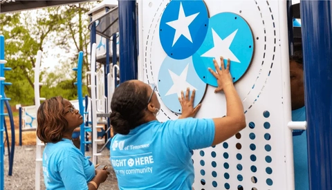 Volunteers attach a star‑themed activity panel to an outdoor playground structure as part of a community improvement project.