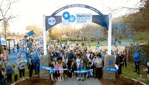 Community members gather under a BlueCross Healthy Place arch at St. Elmo Park during a ribbon‑cutting celebration with blue confetti.