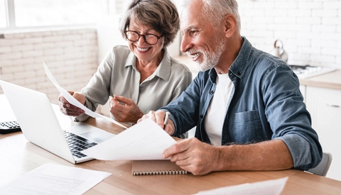 Smiling senior couple using laptop and doing paperwork in kitchen