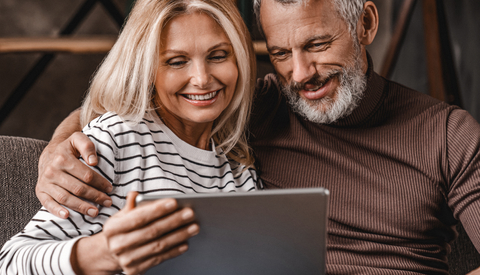 Smiling middle aged couple using digital tablet on sofa at home