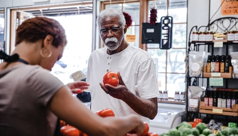 Female grocery clerk helps senior man find best produce selection