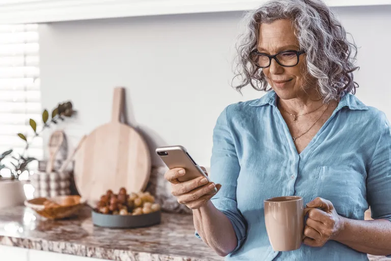 Senior woman standing in the kitchen with her phone