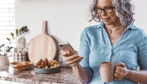 Senior woman standing in the kitchen with her phone