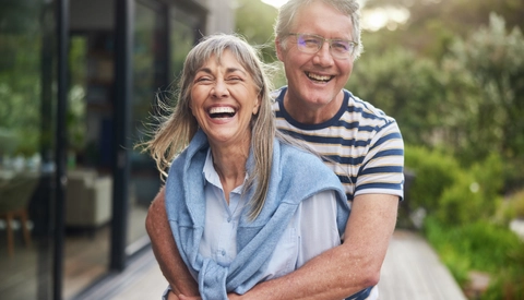 Mature couple standing arm in arm and laughing outside in summer