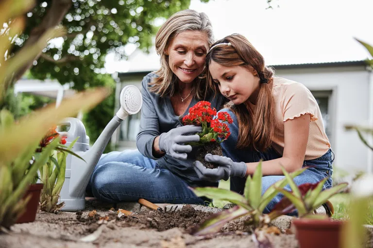 Smiling grandma planting flowers with her granddaughter in a garden