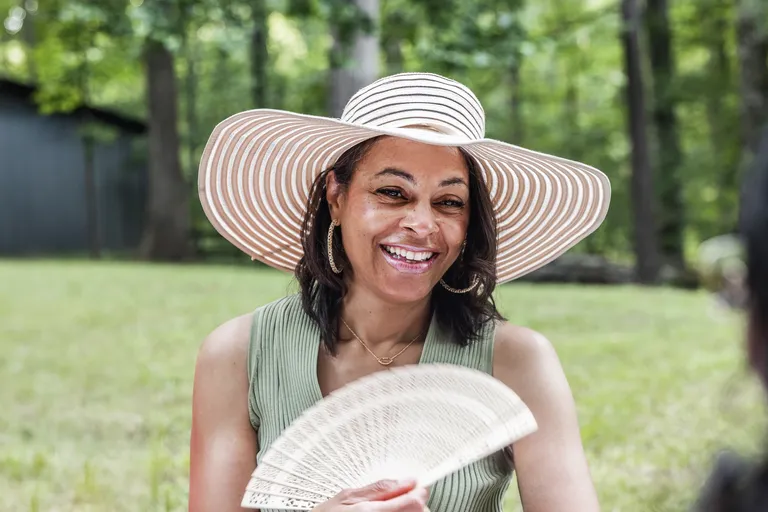Portrait of woman outdoors wearing hat and holding hand fan