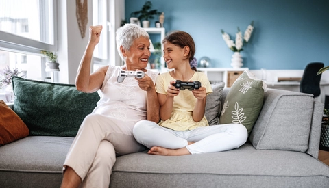 Grandmother and her young granddaughter playing video games together in the living room.