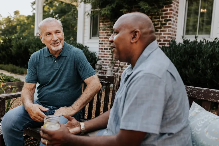 Two men talking and sitting outside in garden chairs.