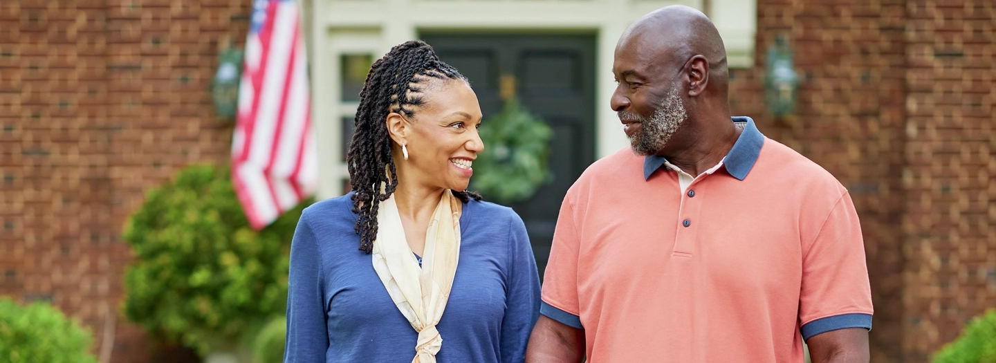 Happy middle aged couple holding hands in their front yard.