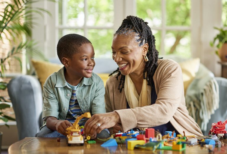 An adult and a child sit together at a table playing with toys and building blocks in a residential living room